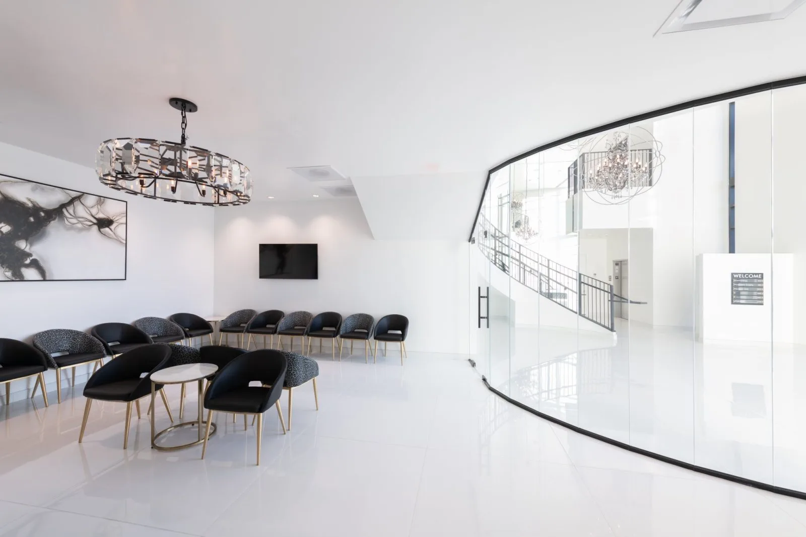 Modern waiting room with black and gray chairs, small side tables, TV screen, and curved glass partition leading to clinical area